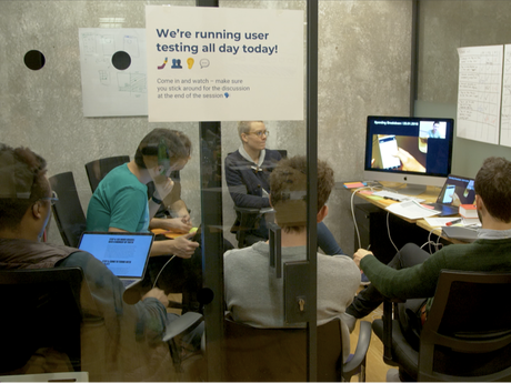Picture of a group of people sitting in a room watching usability testing happening via a monitor